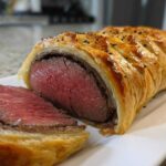A cross-section view of an Individual Beef Wellington for Two showing medium-rare beef wrapped in golden puff pastry.