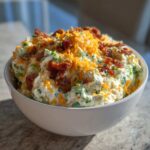 A white bowl filled with creamy Jalapeno Cheddar Million Dollar Dip, topped with shredded cheddar and bacon bits.