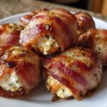 Close-up of several crispy, bacon-wrapped Kielbasa and Cream Cheese Pig Shots piled on a white plate.