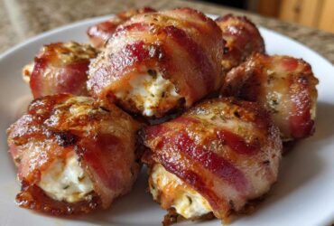 Close-up of several crispy, bacon-wrapped Kielbasa and Cream Cheese Pig Shots piled on a white plate.
