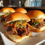 Close-up of three Korean BBQ Beef Sliders topped with shredded carrots and green onions.