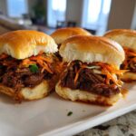 Four delicious Korean BBQ Beef Sliders piled high with shredded beef and bright orange kimchi slaw on soft buns.