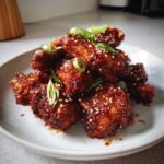 A pile of crispy, glazed Korean Fried Chicken Wings coated in a spicy sauce and sprinkled with sesame seeds and green onions.