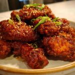 A pile of glossy, dark red Korean Fried Chicken Wings coated in sauce, sprinkled with sesame seeds and green onions.