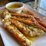 Close-up of cooked Lemon Pepper Dungeness Crab Legs seasoned with herbs and butter, served with a dipping sauce.