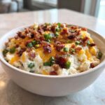 Close-up of a white bowl filled with creamy Loaded Baked Potato Dip, topped with shredded cheddar, bacon bits, and green onions.