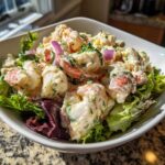 A bowl filled with rich Lobster Tail Salad with Lemon Mayo Dressing, chunks of lobster meat, red onion, and fresh greens.