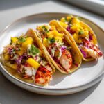 Three delicious Lobster Tail Tacos filled with grilled lobster meat, purple cabbage slaw, and topped with bright yellow mango chunks.