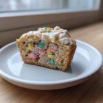 A close-up cross-section of a Lucky Charms Cereal Milk Muffin showing colorful marshmallows baked inside.