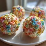 Four colorful Lucky Charms Popcorn Balls made with marshmallows displayed on a white plate.