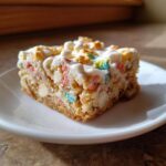 A close-up of one square Lucky Charms White Chocolate Blondies bar with white frosting and colorful marshmallows.