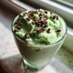 Close-up of bright green Mint Chocolate Chip Shamrock Mousse topped with chocolate shavings in a glass.
