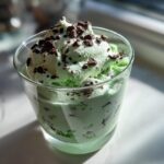 A glass filled with light green Mint Chocolate Chip Shamrock Mousse topped with chocolate shavings.
