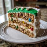 A thick slice of Monster Cookie Football Cake showing layers of cookie dough, white frosting, and colorful M&Ms.