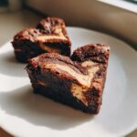 Two fudgy, heart-shaped Nutella Swirl Brownie Hearts with a visible creamy swirl on a white plate.
