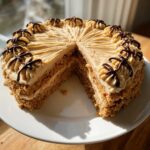 A slice removed from a layered Oatmeal Raisin Football Cookie Cake with tan frosting and chocolate drizzle.