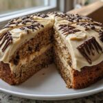 A large slice cut from an Oatmeal Raisin Football Cookie Cake, showing layers and light brown frosting with chocolate drizzle.