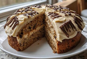A large slice cut from an Oatmeal Raisin Football Cookie Cake, showing layers and light brown frosting with chocolate drizzle.