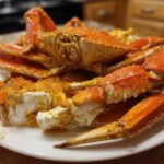 A pile of bright orange crab legs coated in Old Bay Butter Steamed Crab Legs seasoning on a white plate.