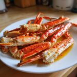 A plate piled high with bright red Old Bay Butter Steamed Crab Legs glistening in savory butter sauce.