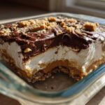 A square slice of rich Dessert 7-Layer Dip (Peanut Butter and Chocolate) showing layers of crust, peanut butter, cream, and chocolate topping.
