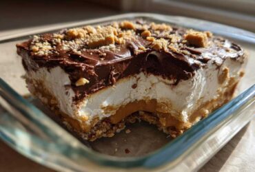 A square slice of rich Dessert 7-Layer Dip (Peanut Butter and Chocolate) showing layers of crust, peanut butter, cream, and chocolate topping.