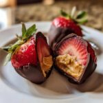 Close-up of Peanut Butter Stuffed Chocolate Strawberries, one cut in half showing creamy peanut butter inside the strawberry.