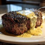 A perfectly cooked Peppercorn Crusted Filet Mignon topped with a creamy, speckled sauce on a white plate.