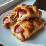 Two golden-brown Pepperoni Pizza Roll Ups showing a dramatic cheese pull between them.