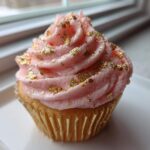 A close-up of a Pink Champagne Cupcakes with Gold Sprinkles, featuring pink frosting and edible gold leaf.