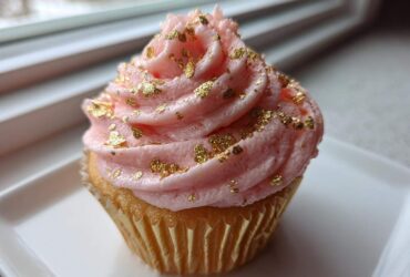 A close-up of a Pink Champagne Cupcakes with Gold Sprinkles, featuring pink frosting and edible gold leaf.