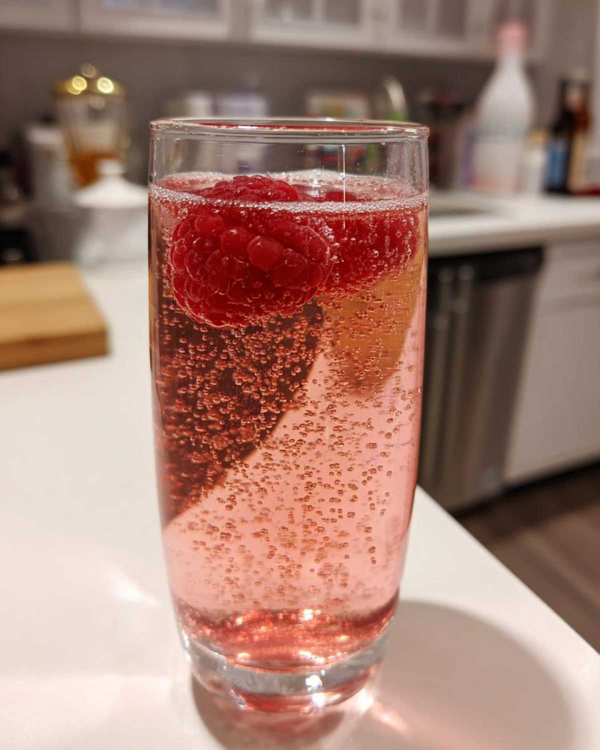 Close-up of a tall glass containing a bubbly, pink French 75 Cocktail garnished with fresh raspberries.