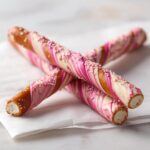 Close-up of Pink White Chocolate Dipped Pretzel Rods featuring a beautiful pink and white marble swirl and pink sprinkles.