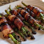 Close-up of cooked Prosciutto Wrapped Asparagus Hearts drizzled with a dark balsamic glaze on a white plate.
