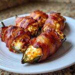 Five crispy Prosciutto Wrapped Jalapeno Poppers filled with melted cheese, served on a white plate.