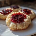 Close-up of soft Raspberry Chia Jam Thumbprint Cookies with bright red jam centers on a white plate.