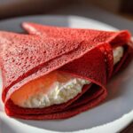 Close-up of two vibrant Red Velvet Crepes with Sweet Cream Cheese Filling folded on a white plate.