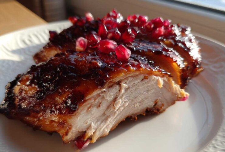 Close-up of sliced Roasted Chicken with Pomegranate Glaze showing juicy white meat and shiny topping.
