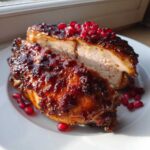 A juicy piece of Roasted Chicken with Pomegranate Glaze, sliced open to show the white meat, topped with glistening glaze and fresh pomegranate seeds.