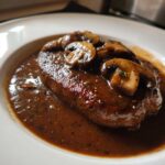 Close-up of a perfectly cooked Salisbury steak smothered in dark, rich mushroom gravy and sliced mushrooms.