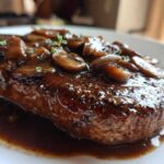 Close-up of a perfectly cooked Salisbury steak smothered in rich mushroom gravy and fresh thyme.