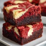 Two stacked, rich Salted Caramel Red Velvet Brownies featuring a dark chocolate base and a vibrant red top layer swirled with cream cheese.