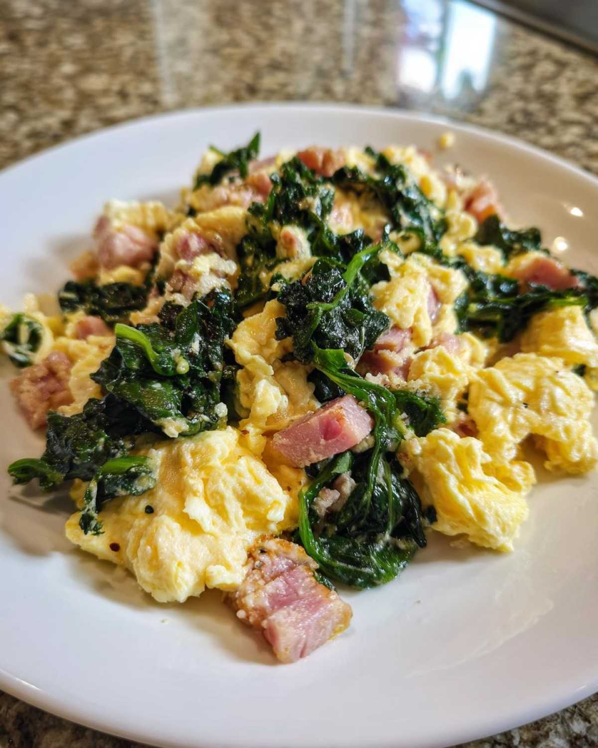 A close-up of fluffy Scrambled Eggs with Kale and Minced Ham served on a white plate.