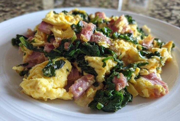 Fluffy scrambled eggs with dark green kale and pink minced ham served on a white plate.