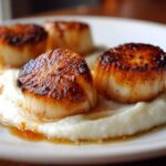 Close-up of perfectly seared scallops resting on a bed of creamy cauliflower puree with pan sauce.