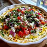 Close-up of Seven-Layer Mediterranean Dip topped with feta, tomatoes, olives, and herbs.