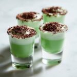 Four green Shamrock Shake Boozy Shooters topped with whipped cream and chocolate shavings.
