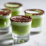 Close-up of Shamrock Shake Boozy Shooters in shot glasses with a white foam top and chocolate shavings.