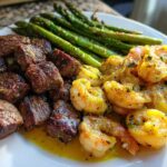 A plate featuring steak bites, garlic butter shrimp, and roasted asparagus, showcasing the Sheet Pan Steak and Garlic Butter Shrimp recipe.