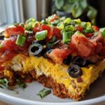 A close-up slice of Vegan 7-Layer Dip showing layers of cashew queso, beans, salsa, olives, and green onions.